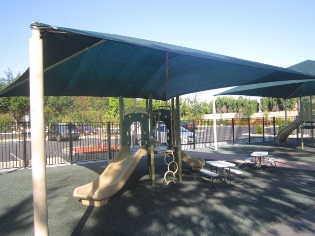 Playground with slides and climbing structures under a large shade canopy