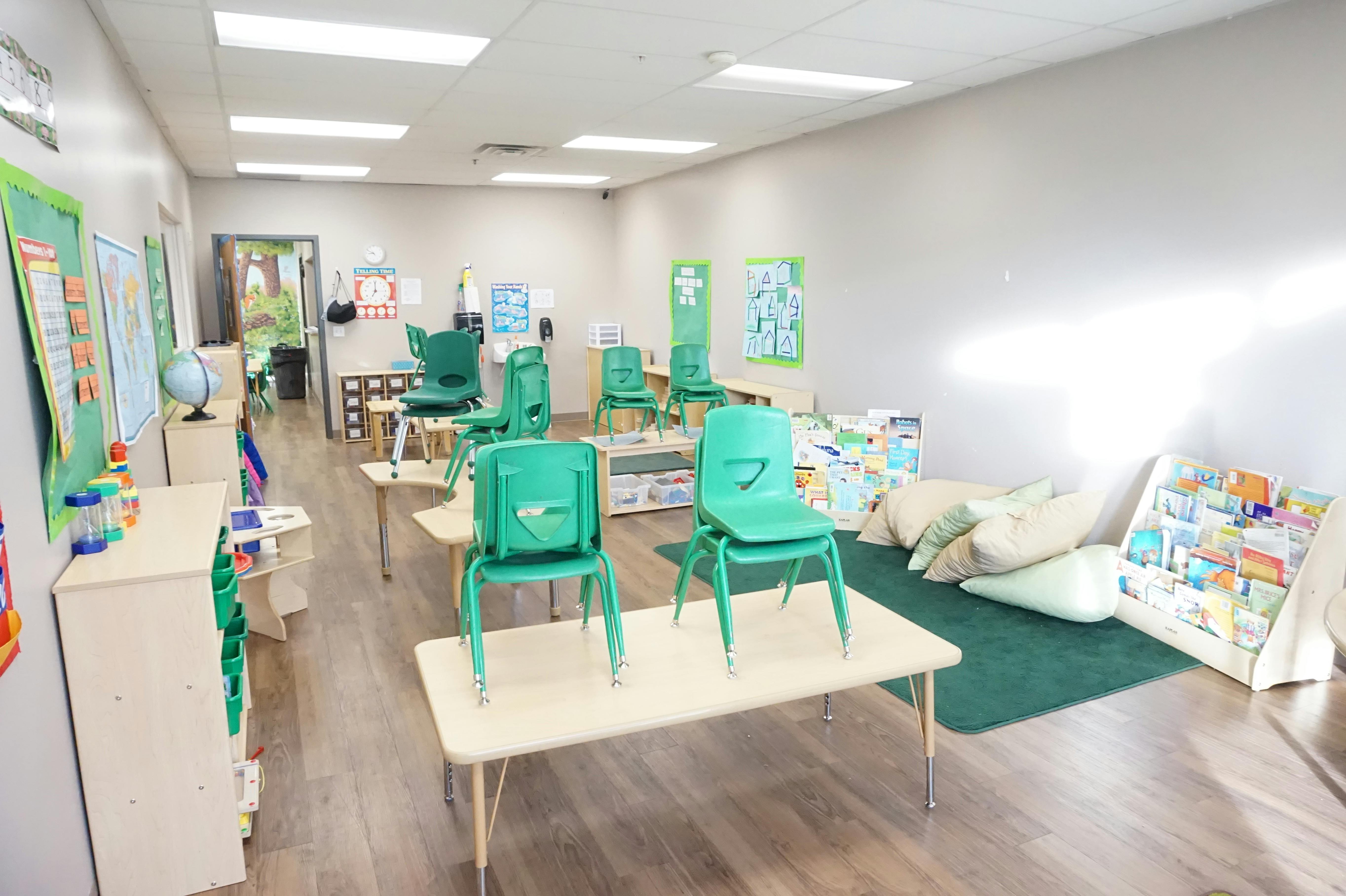 Classroom with small green chairs and tables, reading nook with pillows