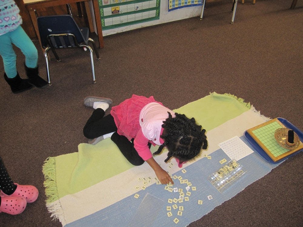 Child lying on a rug, playing with small square tiles