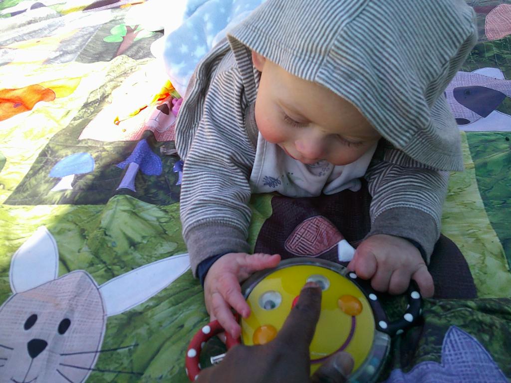 Child lying on a patterned blanket touching a yellow toy