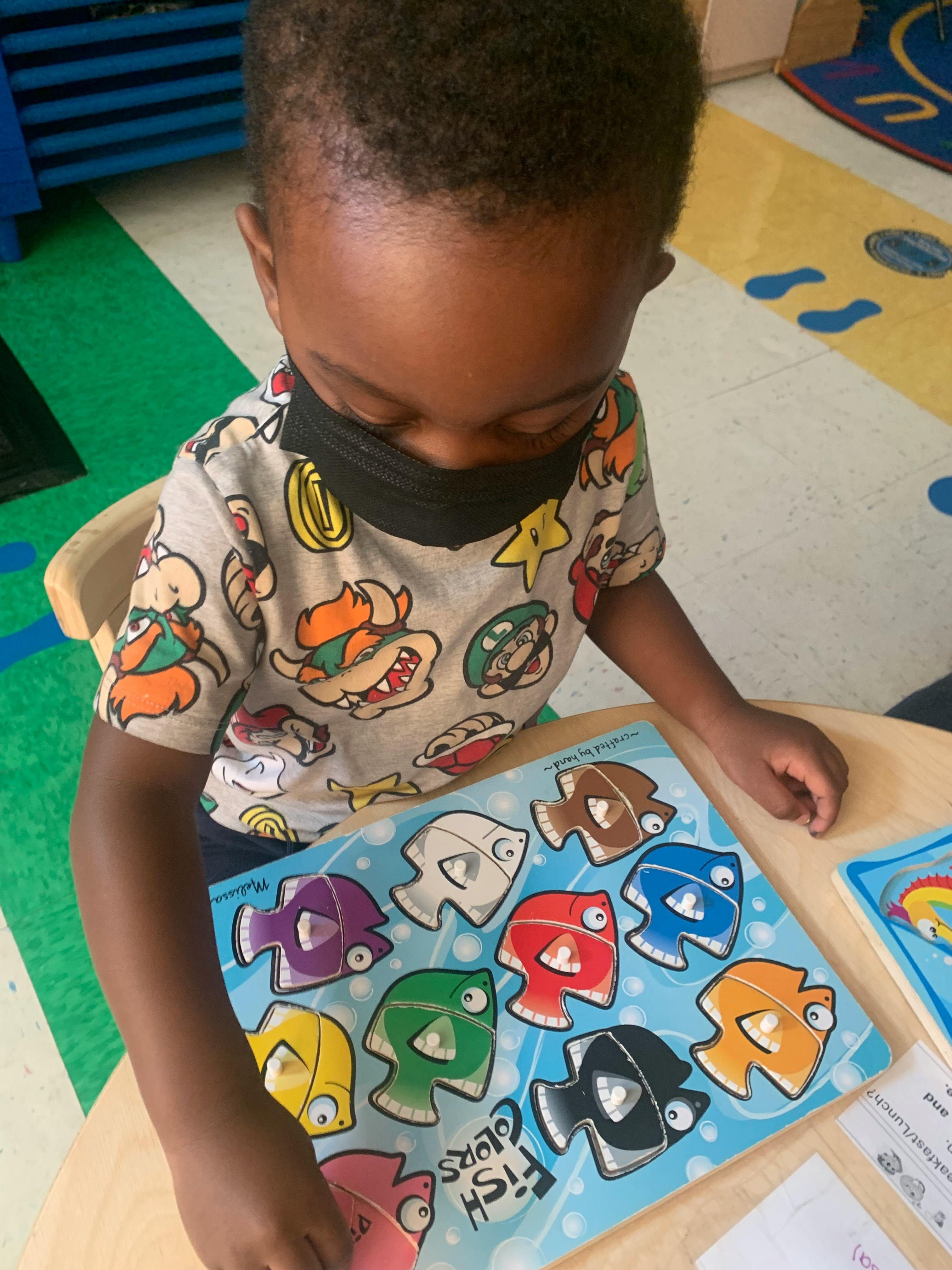 Child in a mask playing with a fish-themed puzzle