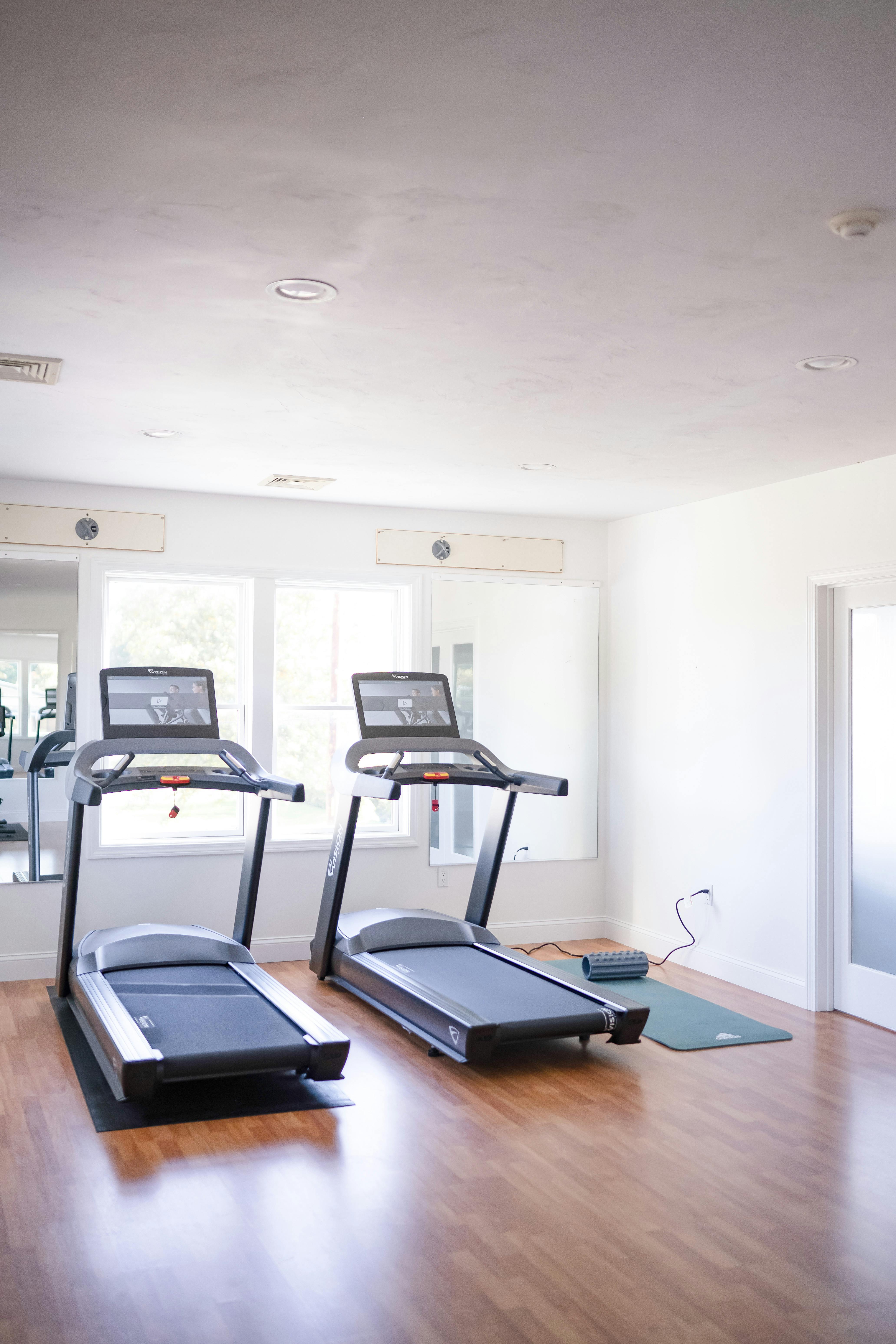 Two treadmills in a room with a yoga mat on the floor