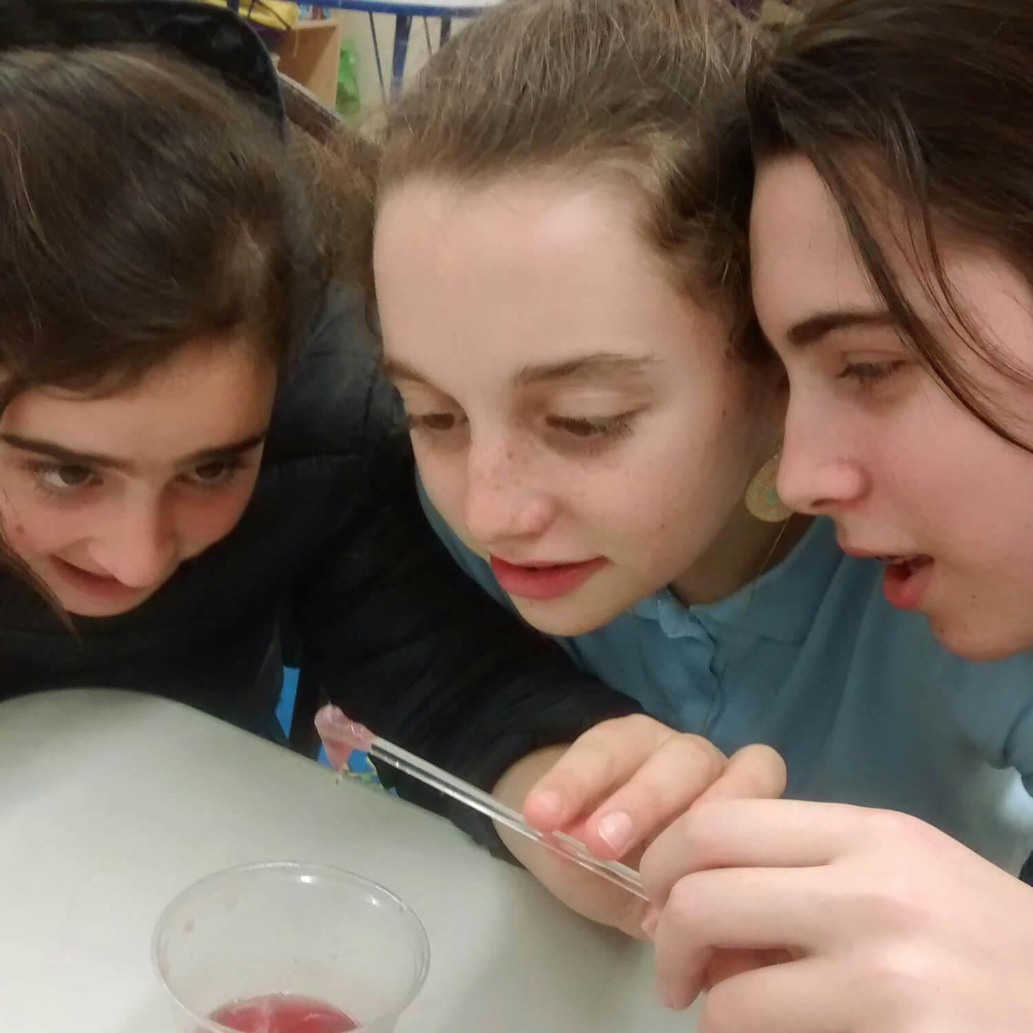 Three teens observing a specimen with tweezers over a cup