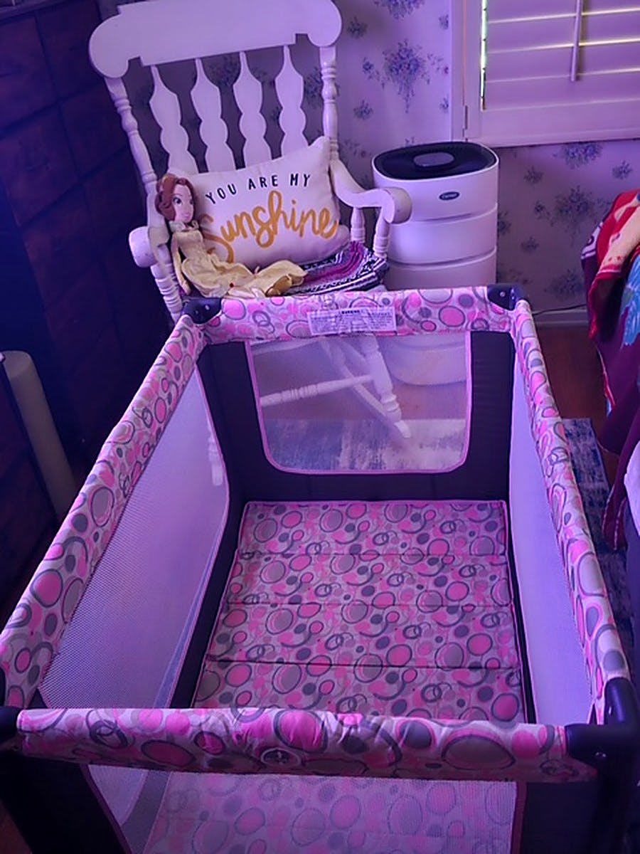 A portable playpen in a room with a rocking chair and a doll