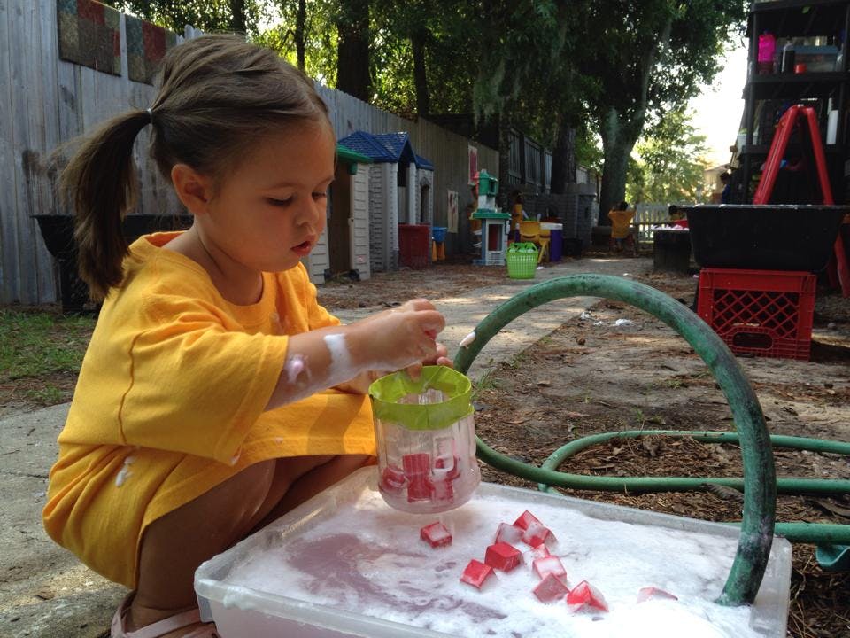 Child playing with water and red blocks in a container outdoors