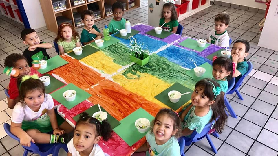Children sitting around a table with a colorful tablecloth in-progress art project