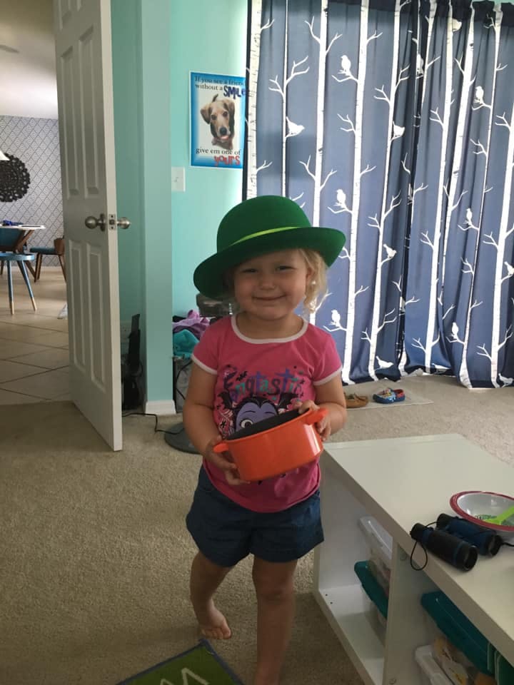 Child wearing a green hat and holding an orange toy pot
