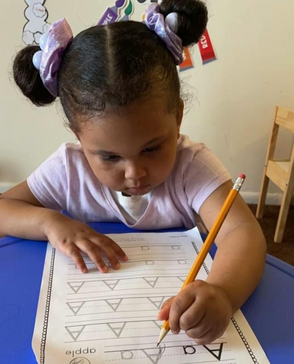 Child writing the letter A on a worksheet with a pencil
