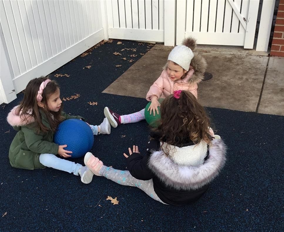 Three children sitting on the ground playing with balls