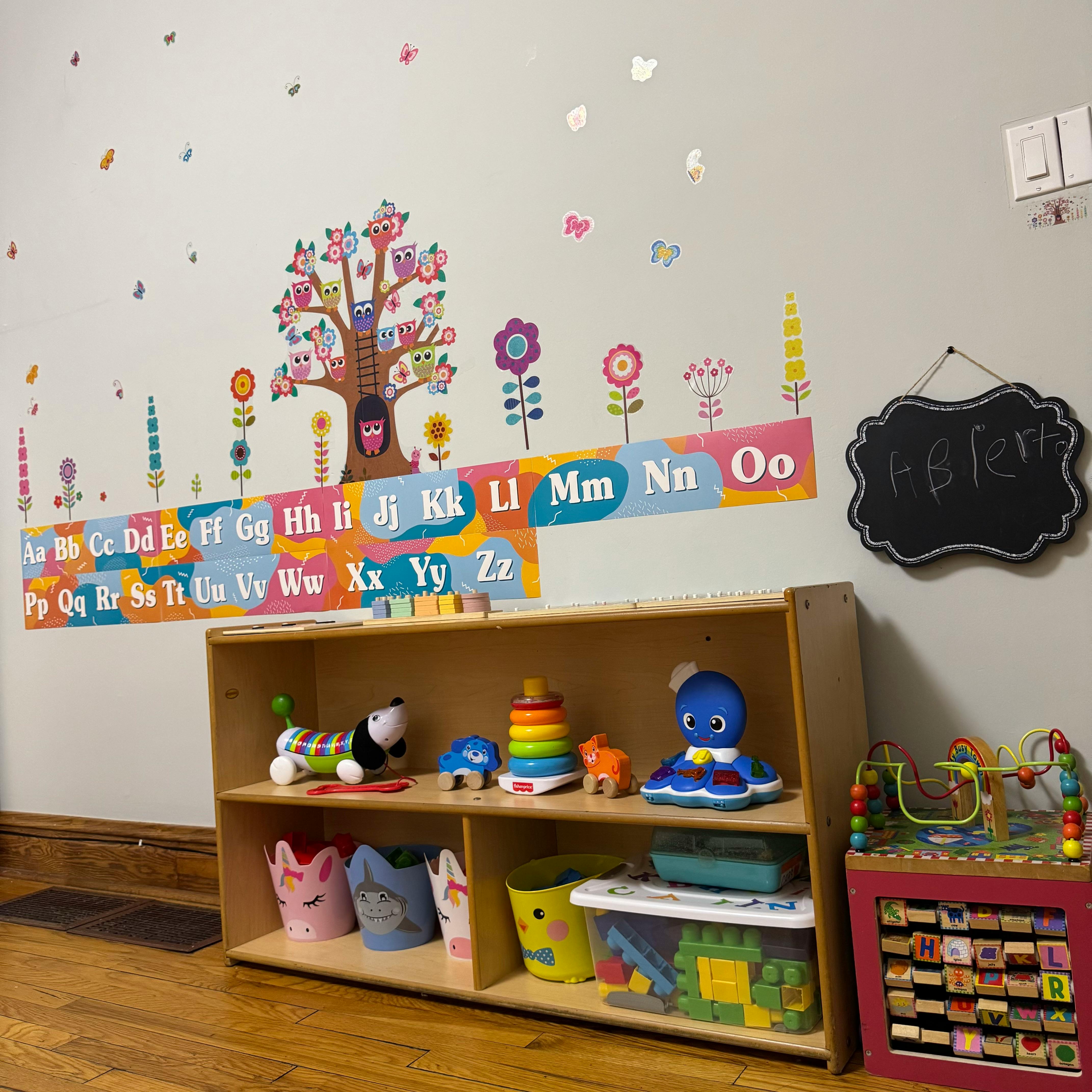 Wall with alphabet chart, tree and flower decals, and a toy shelf