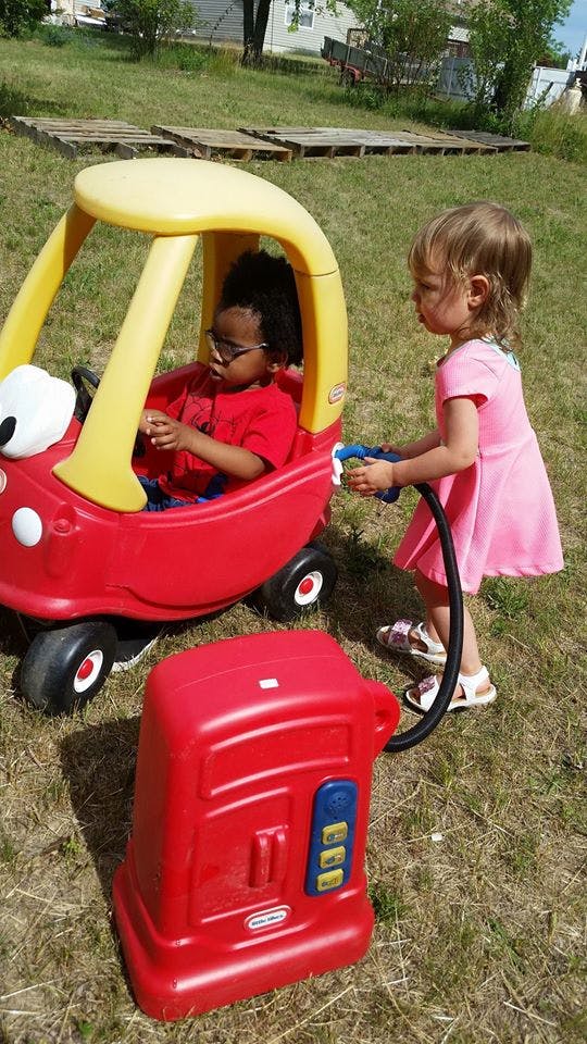 Child in toy car and child using toy gas pump