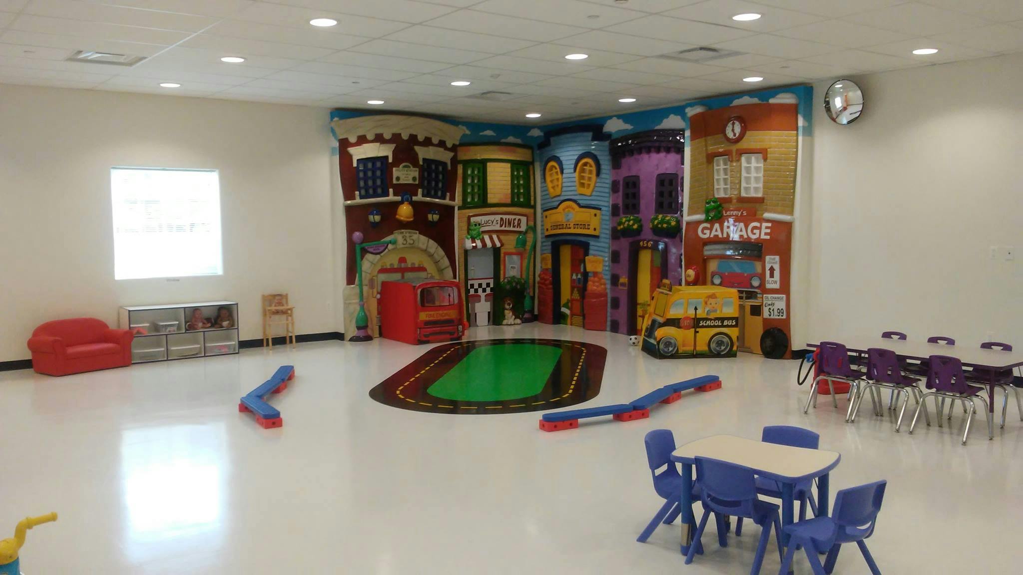 Playroom with colorful wall mural, small tables and chairs, and a red couch
