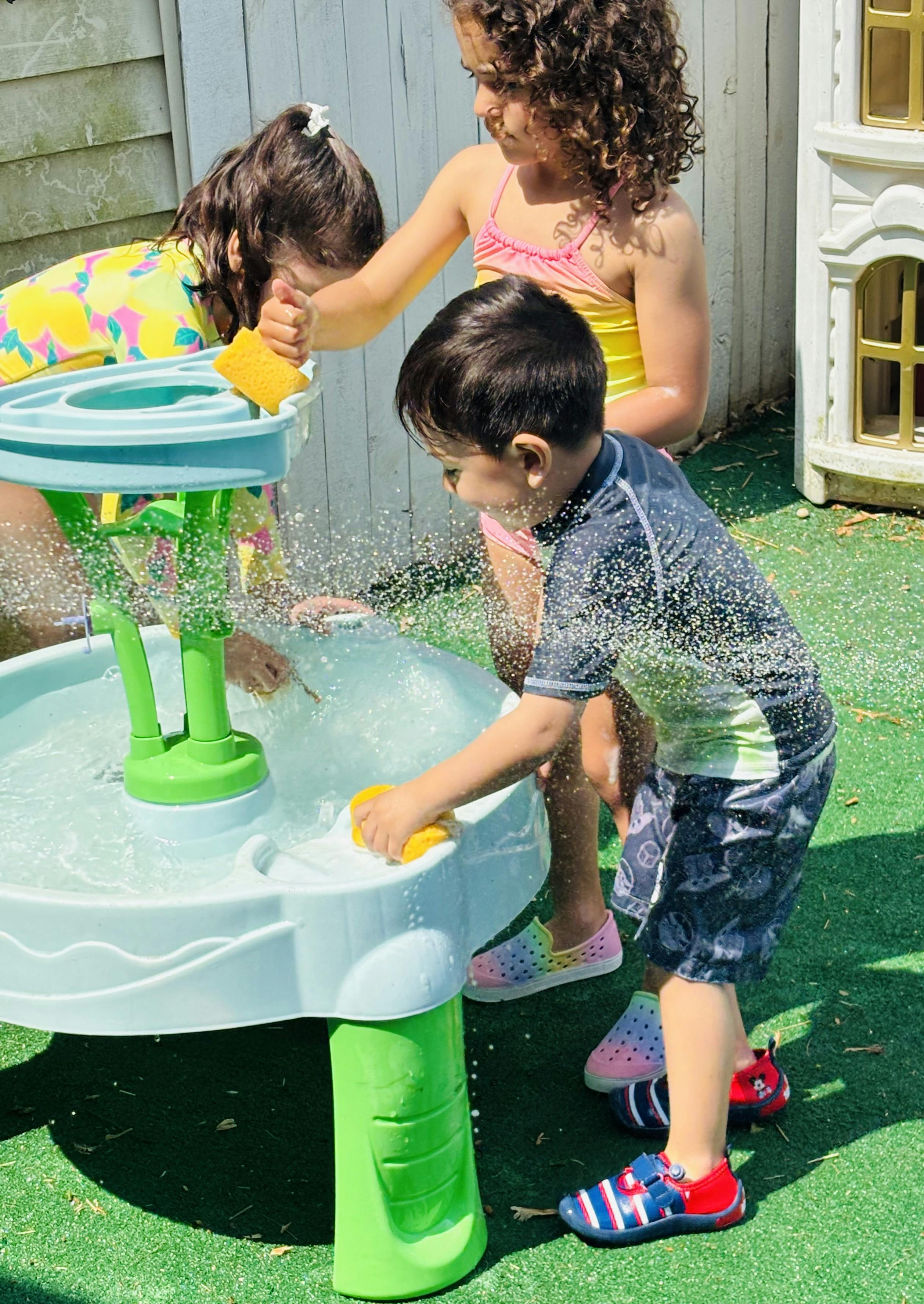 Three children playing with water table, splashing water