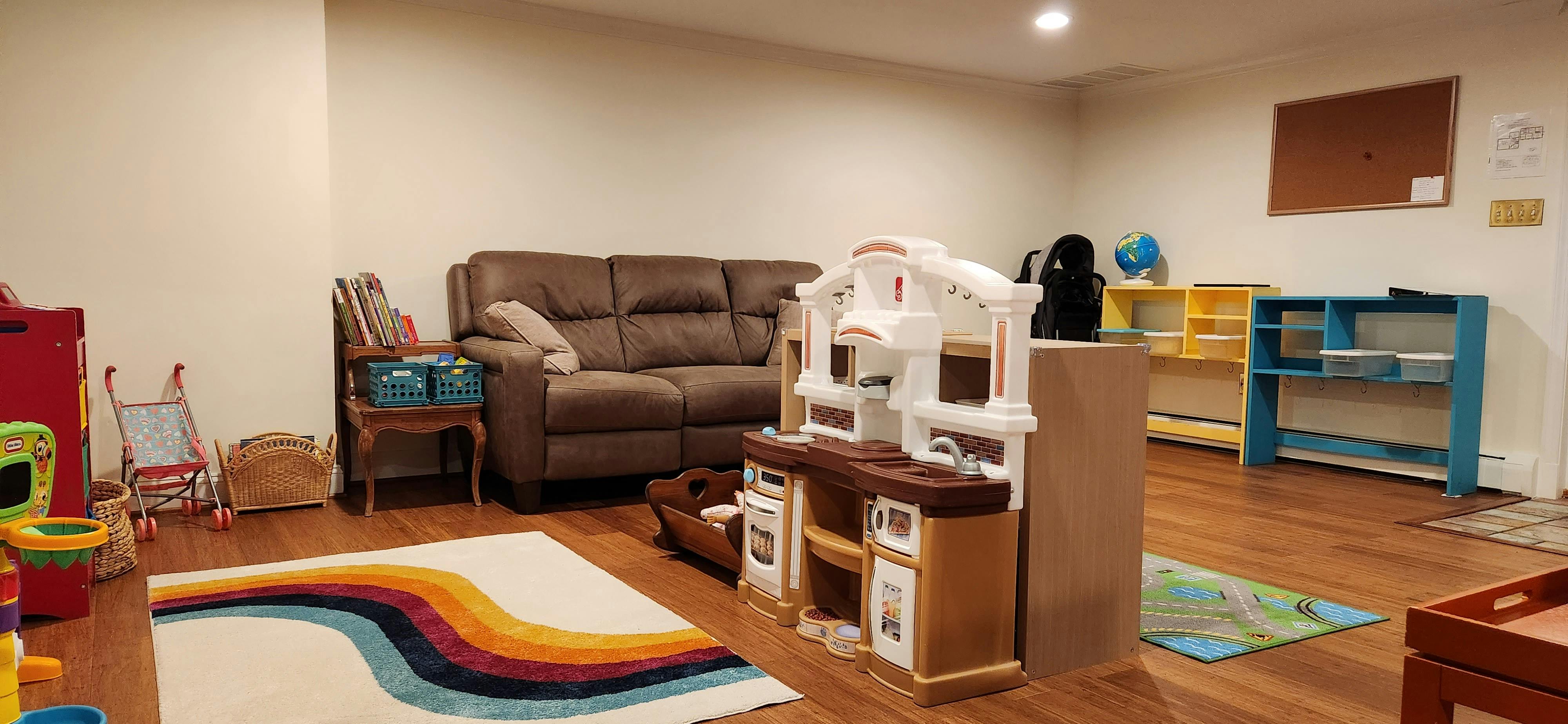 Playroom with a brown sofa, play kitchen, and colorful rug