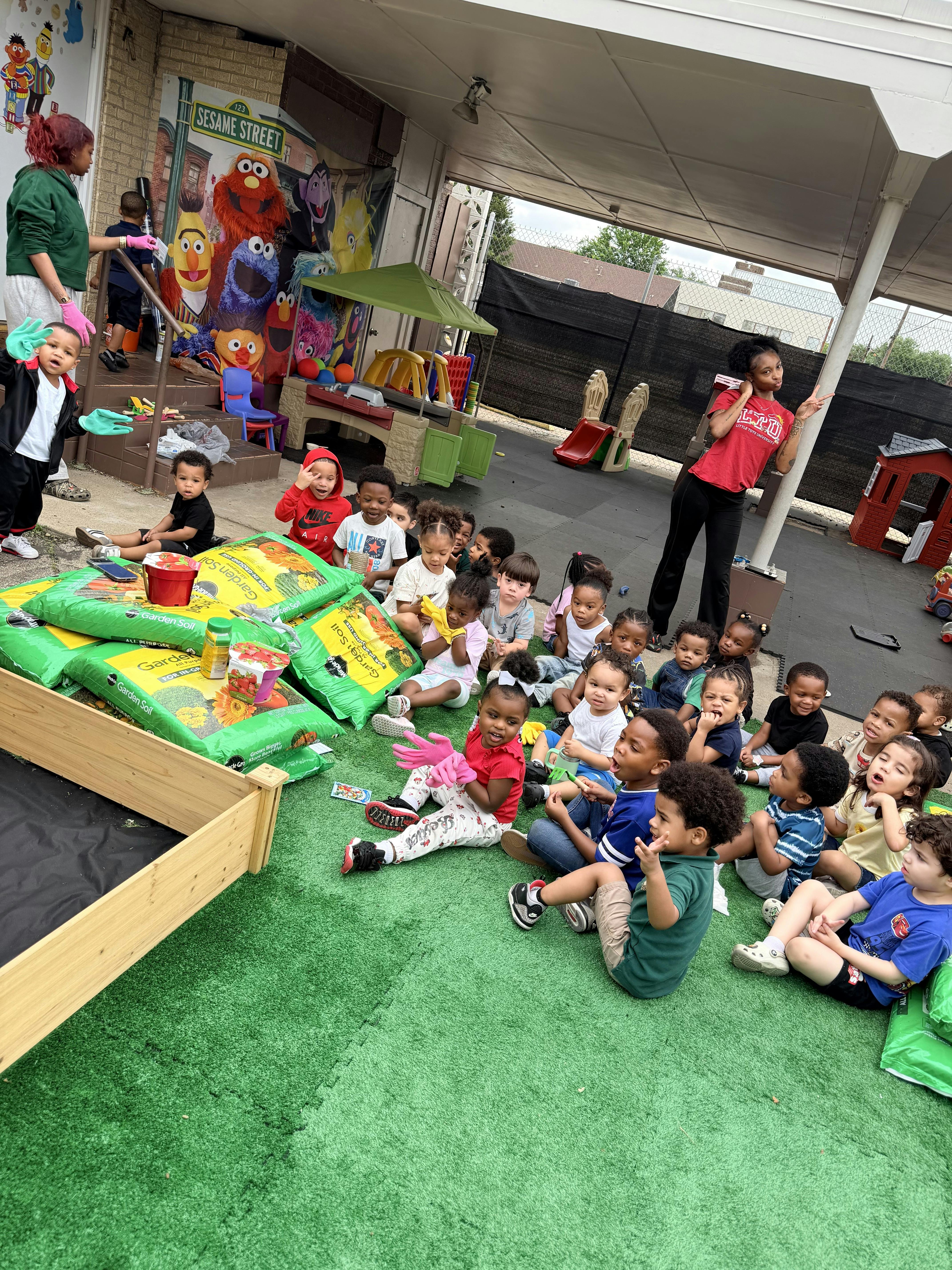 Children sitting on an outdoor rug with bags of potting soil