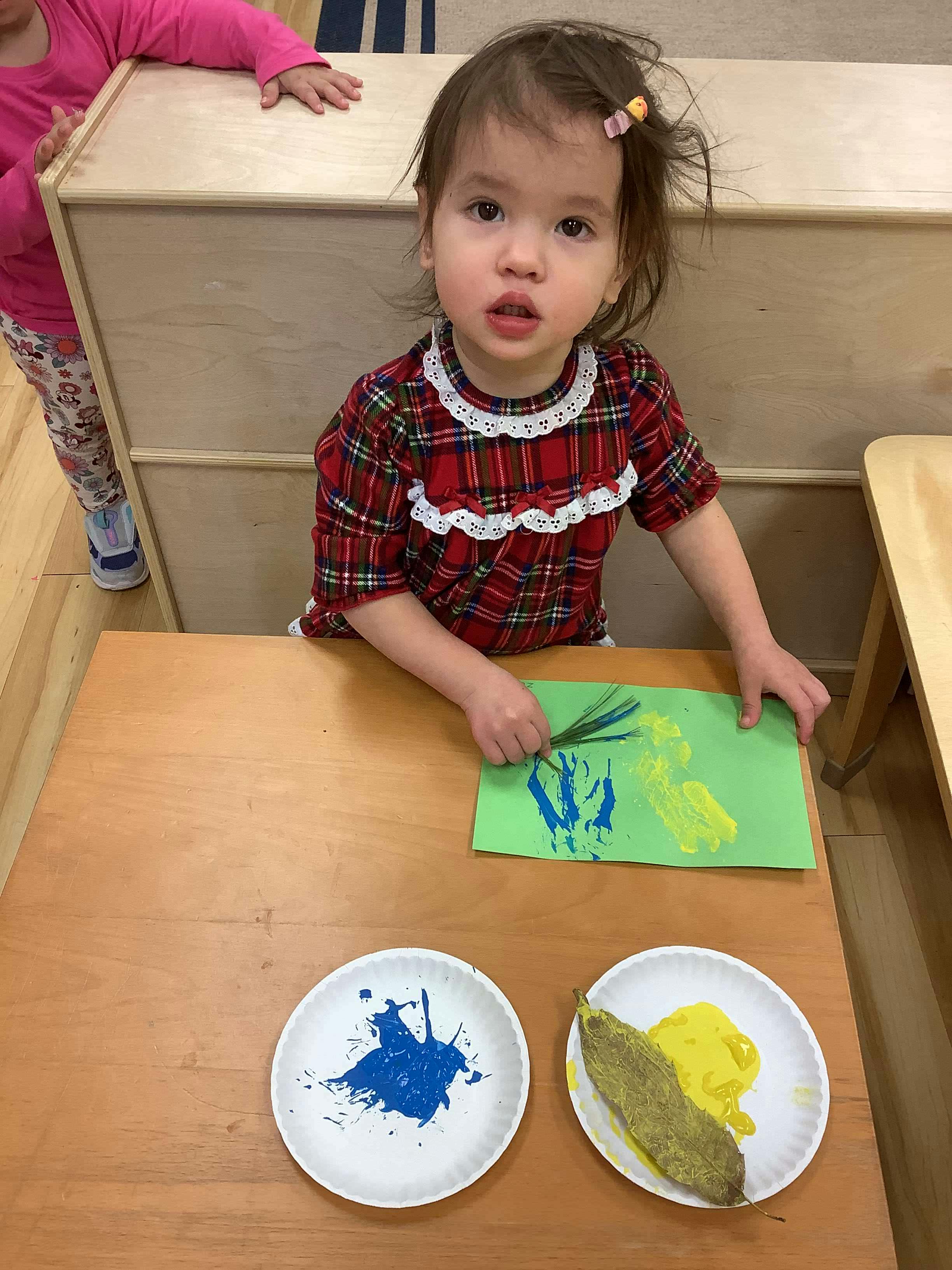Child painting on paper using a leaf and pine needles