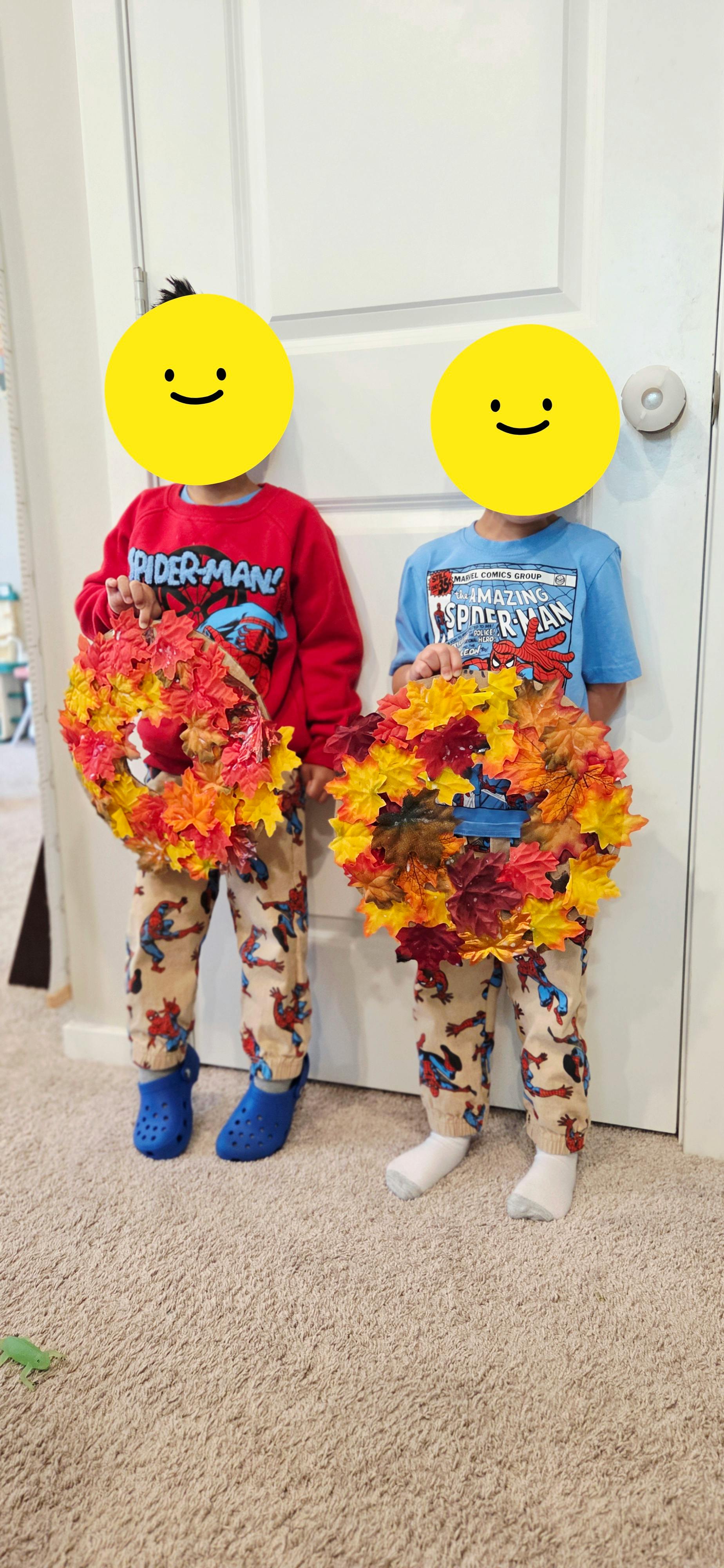 Two children standing and holding handmade autumn leaf wreaths