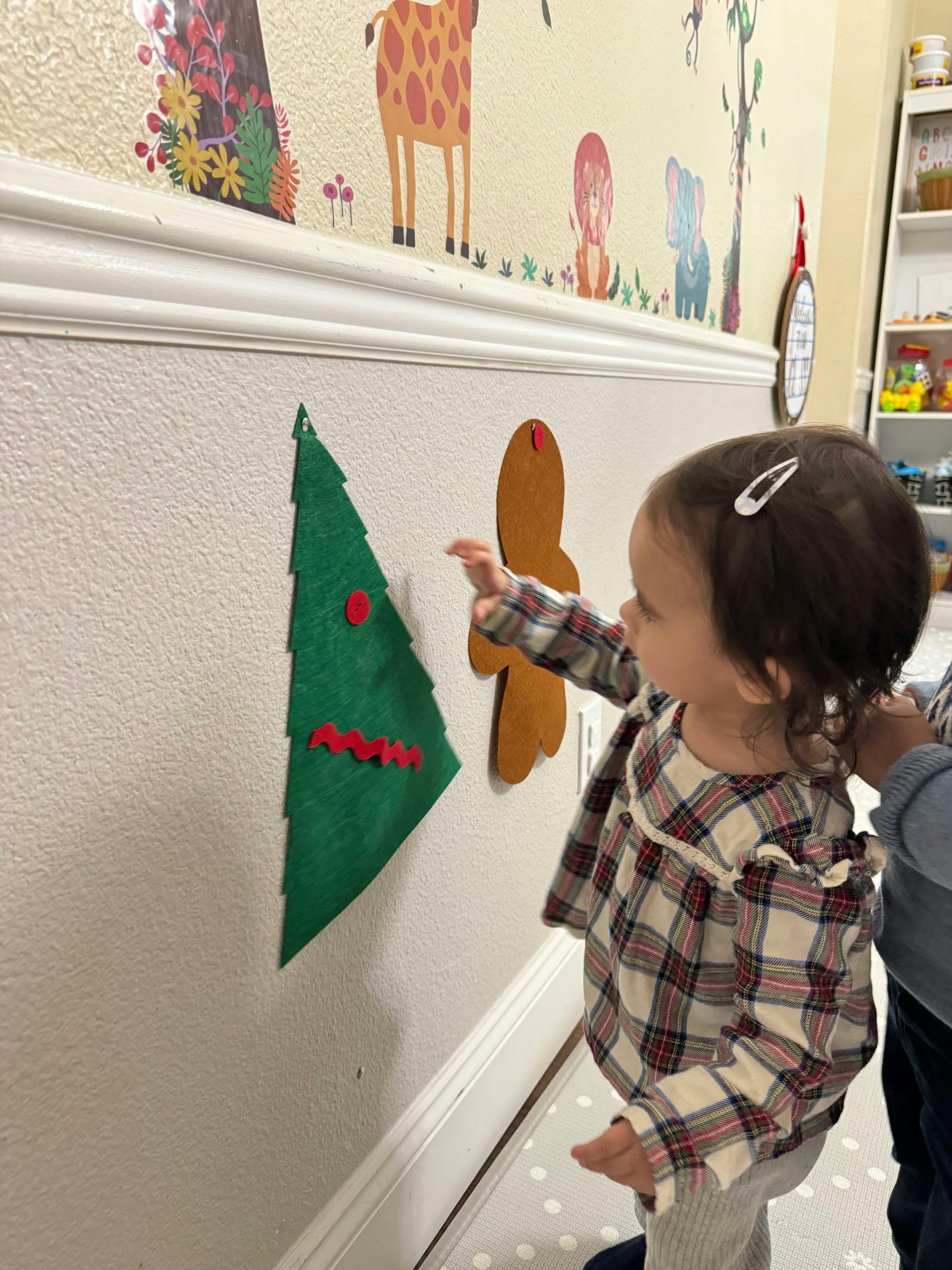 Child touching a felt Christmas tree decoration on a wall