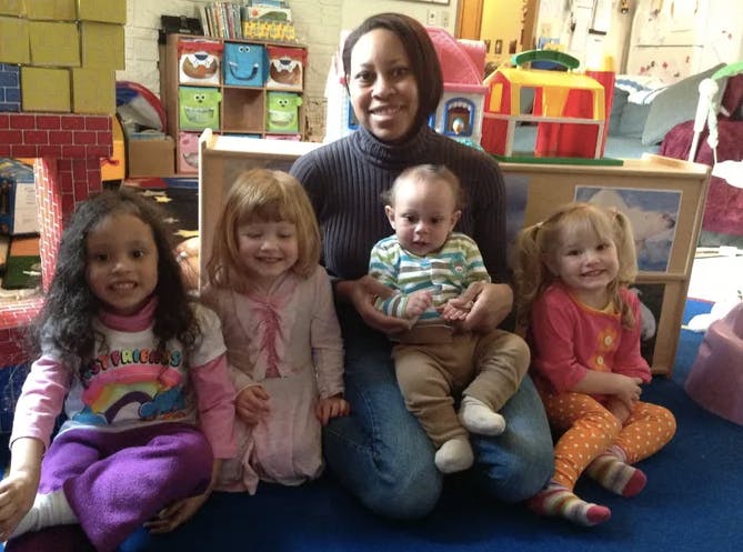 Person holding a baby, with three children sitting nearby in a classroom