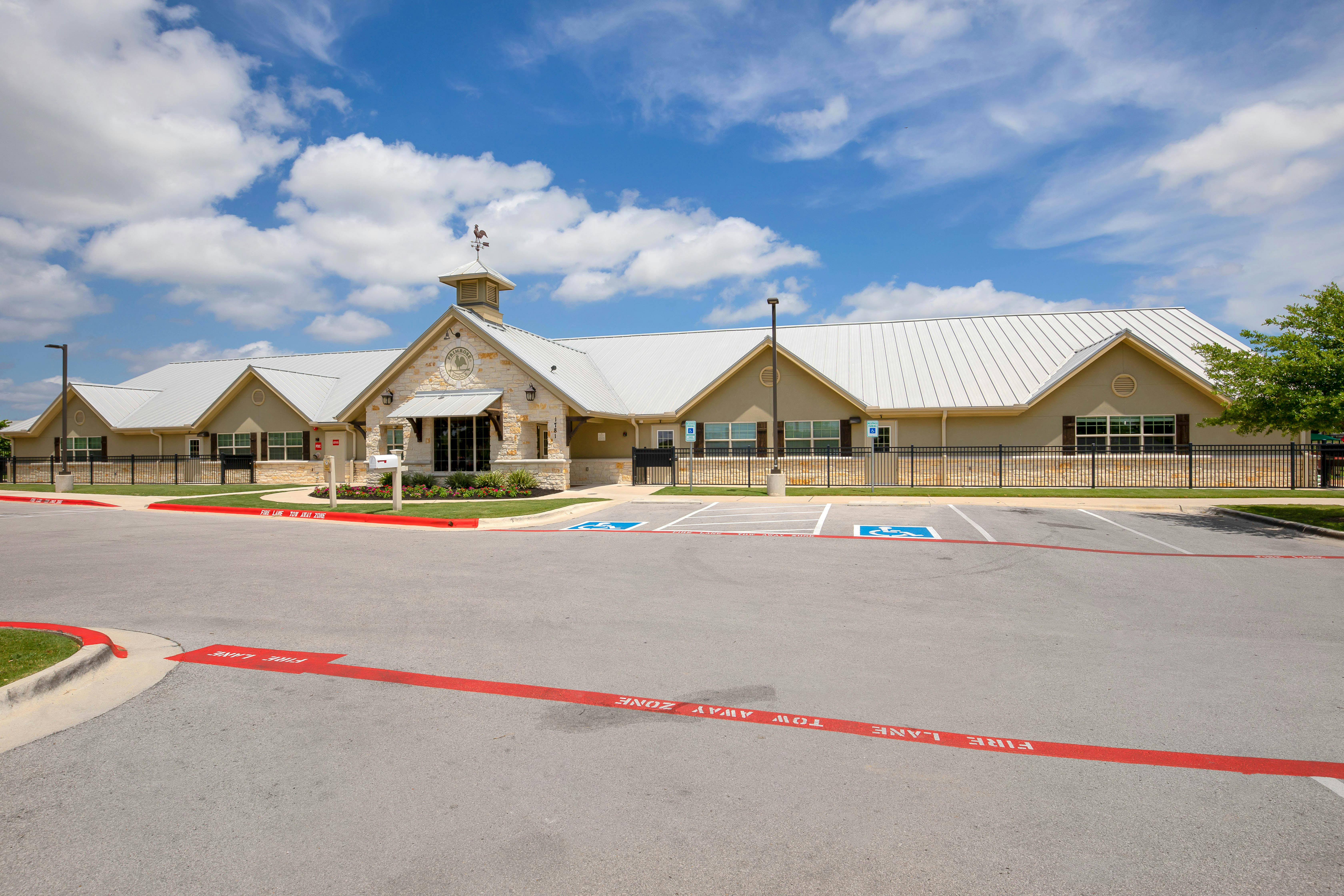 A beige building with a white metal roof and a cupola, with a parking lot in front