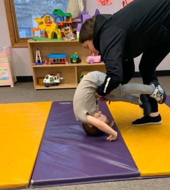 Adult helping child do a headstand on a mat