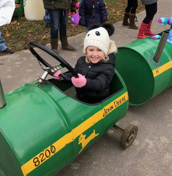 Child in a green barrel train car with "John Deere" written on the side