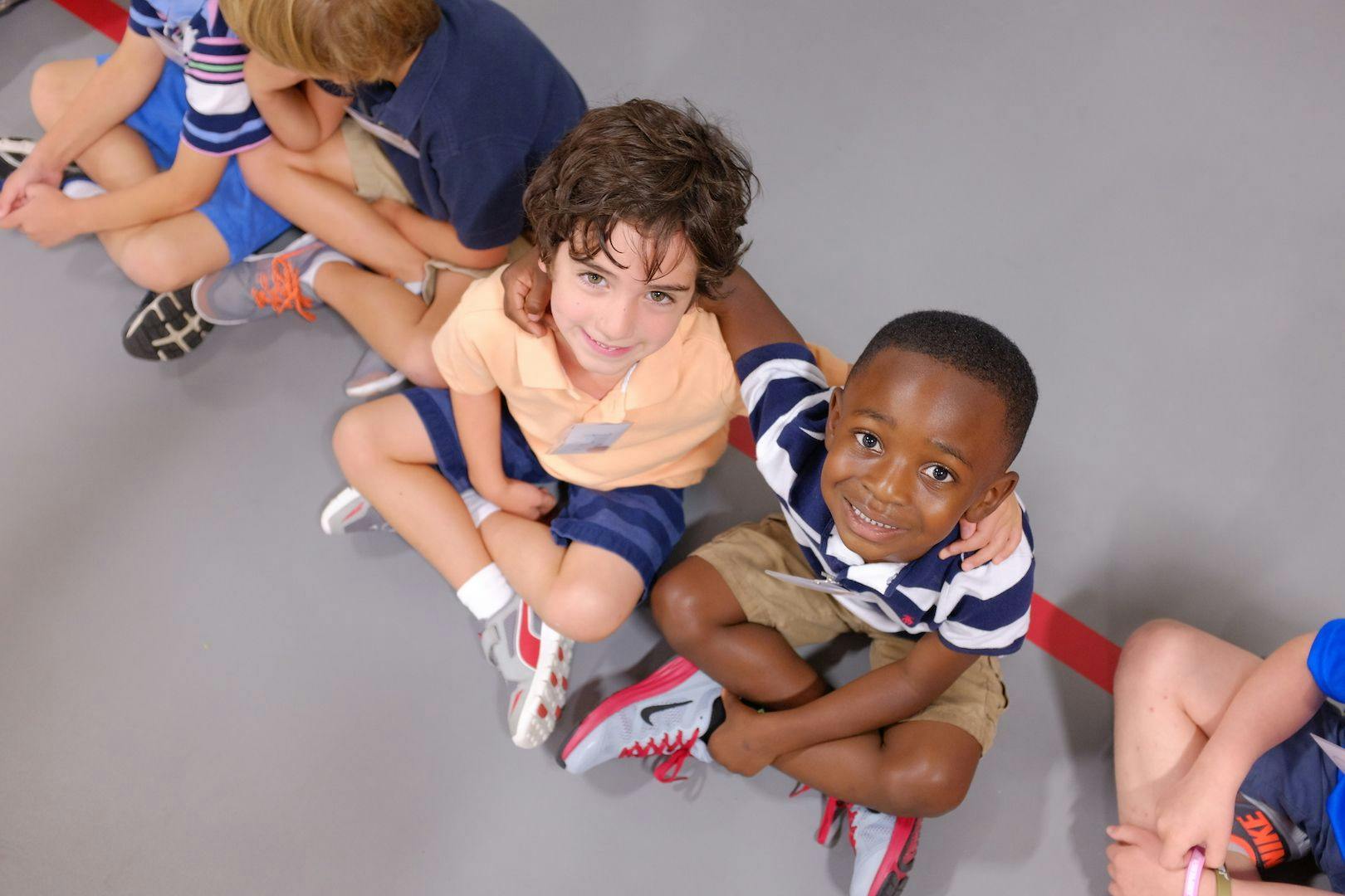 Children sitting in a line on a floor, one child has arm around another