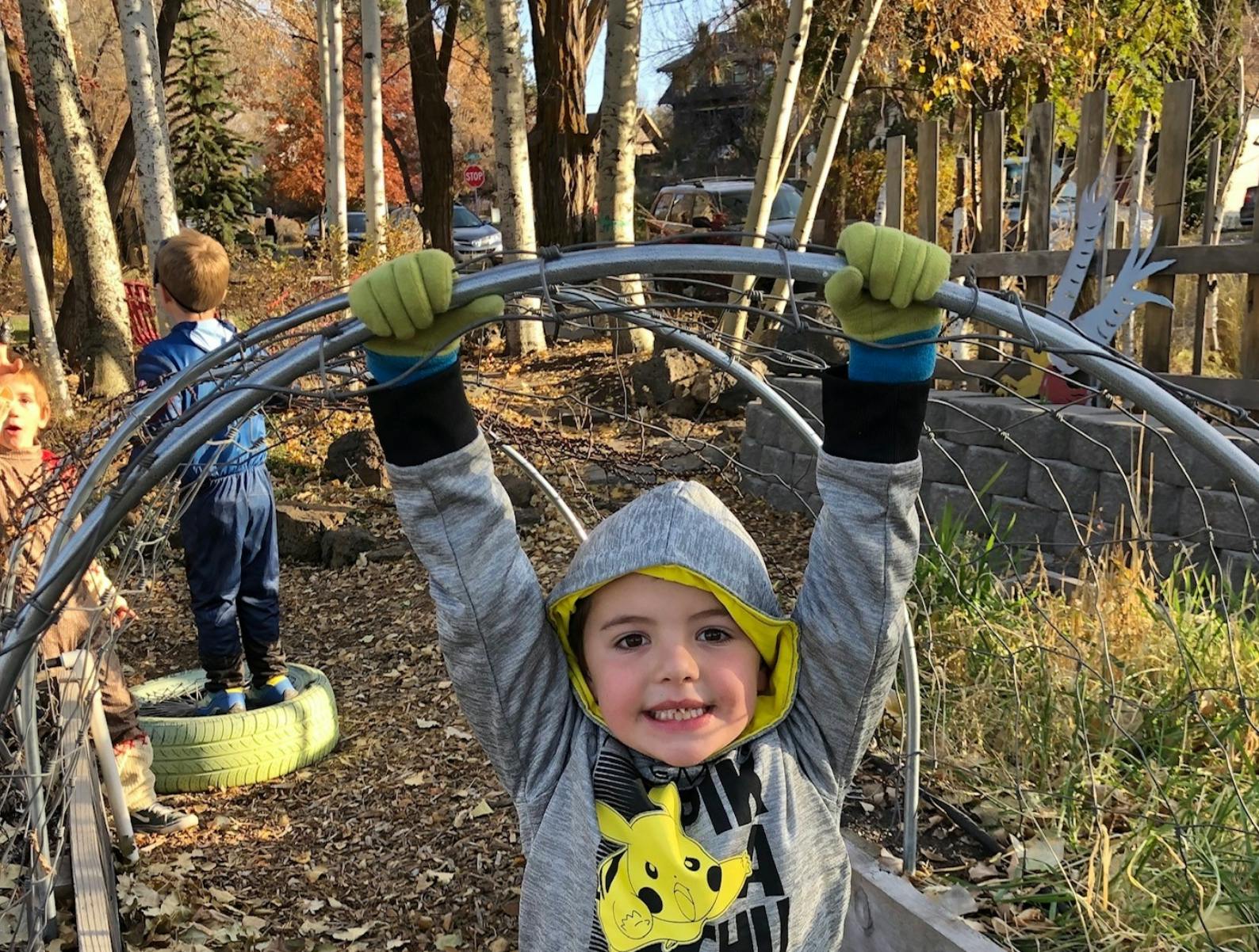 Child in a hooded sweatshirt holding onto a metal arch