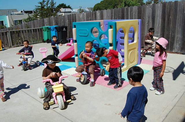Children playing on tricycles and a play structure outdoors