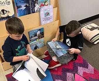 Two children reading books on the floor next to a bookshelf