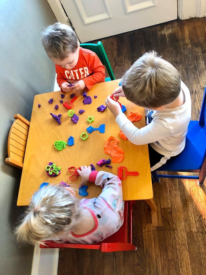 Three children playing with colorful playdough at a table