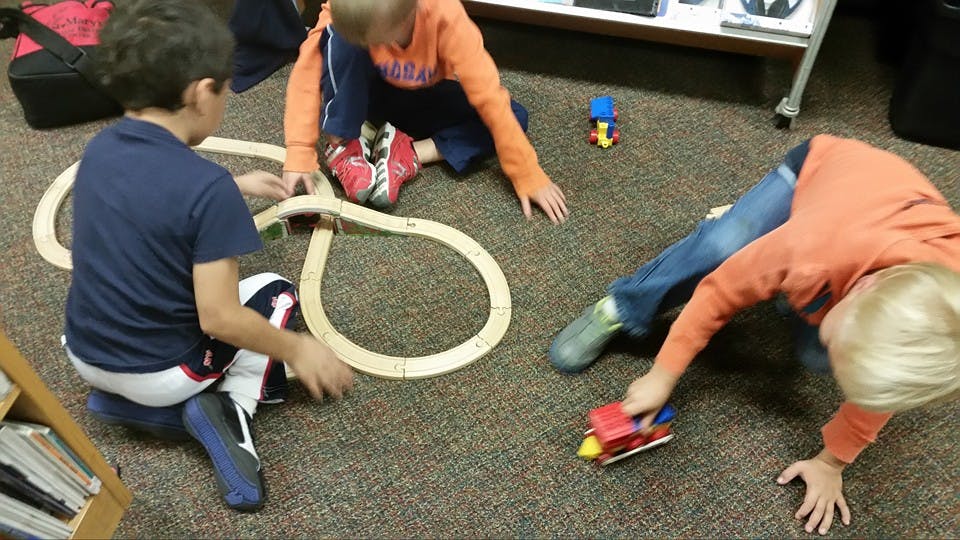 Three children playing with a wooden train track on the floor