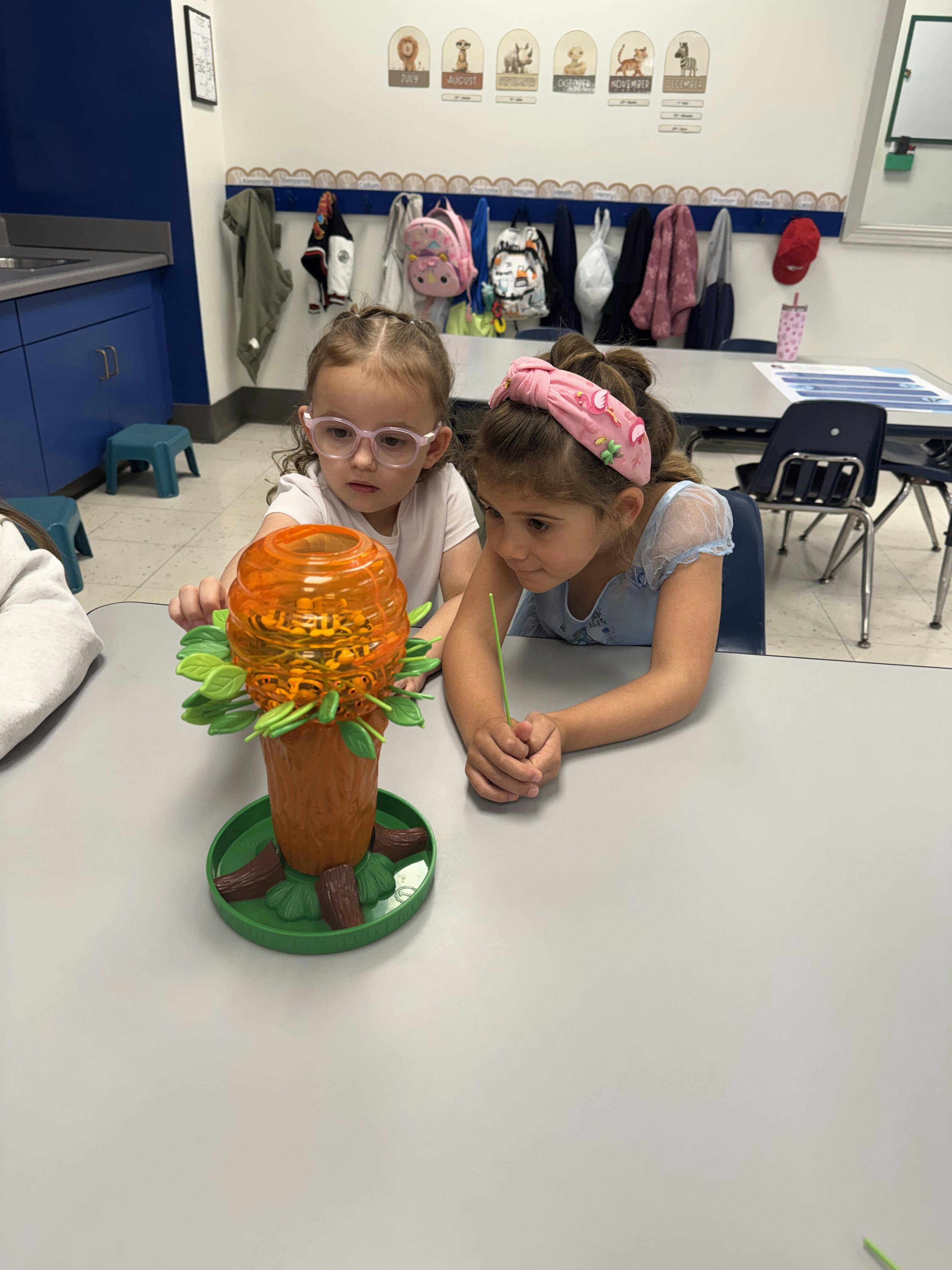 Two children playing a bee-themed tree board game at a table in a classroom