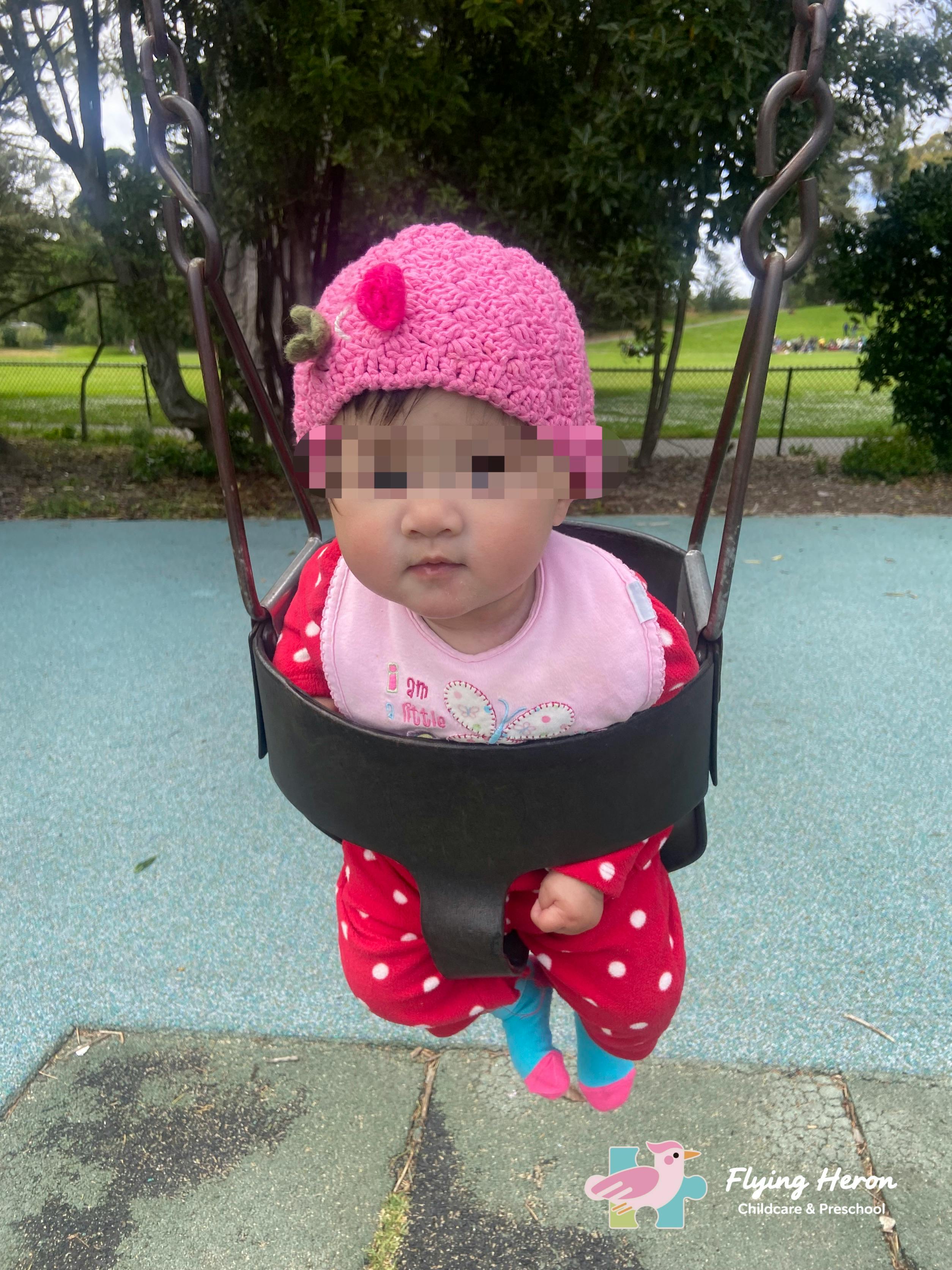 Child in a pink hat and red polka dot outfit sitting in a swing