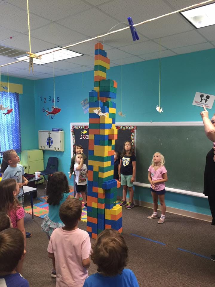 Children looking up at a tall structure made of colorful blocks in a classroom