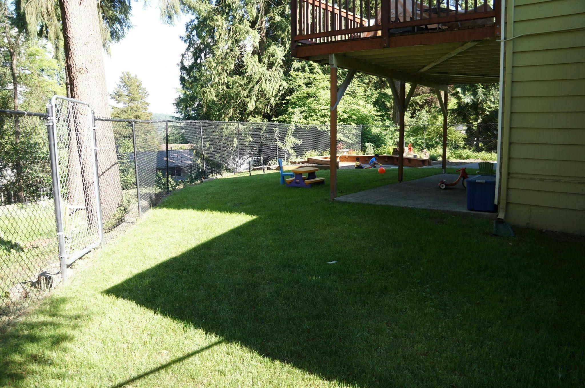 Child playing in a fenced backyard with a patio and lawn