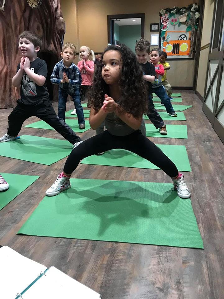 Children doing yoga poses on green mats in a room