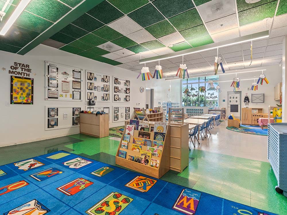 Colorful preschool classroom with tables, chairs, bookshelves, and a large rug