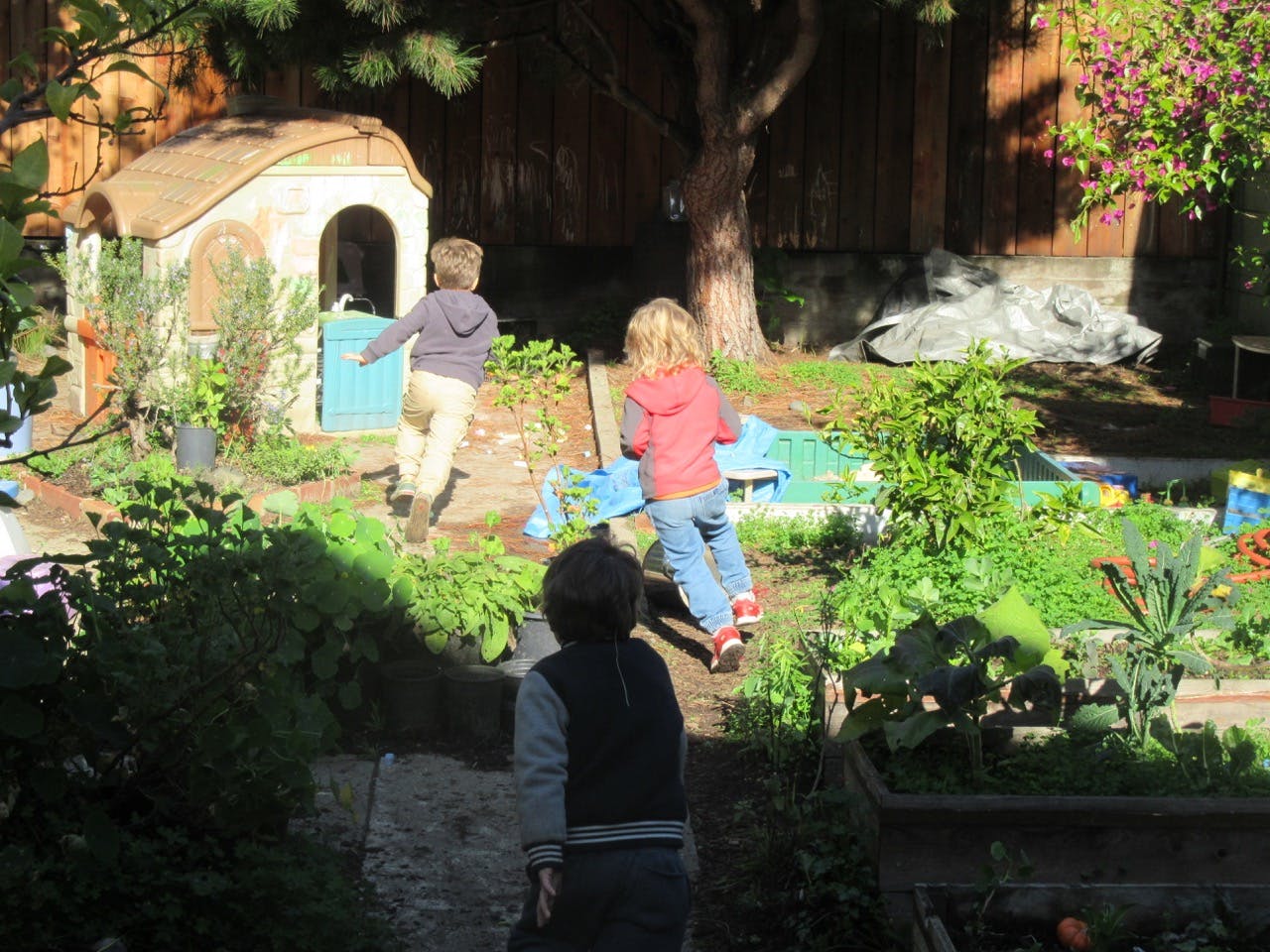 Three children playing in a garden with a small playhouse
