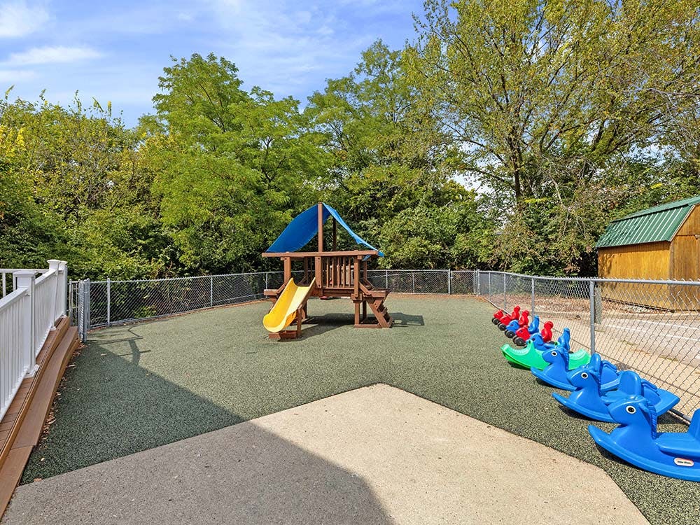 Outdoor playground with a wooden play structure, slide, and riding toys