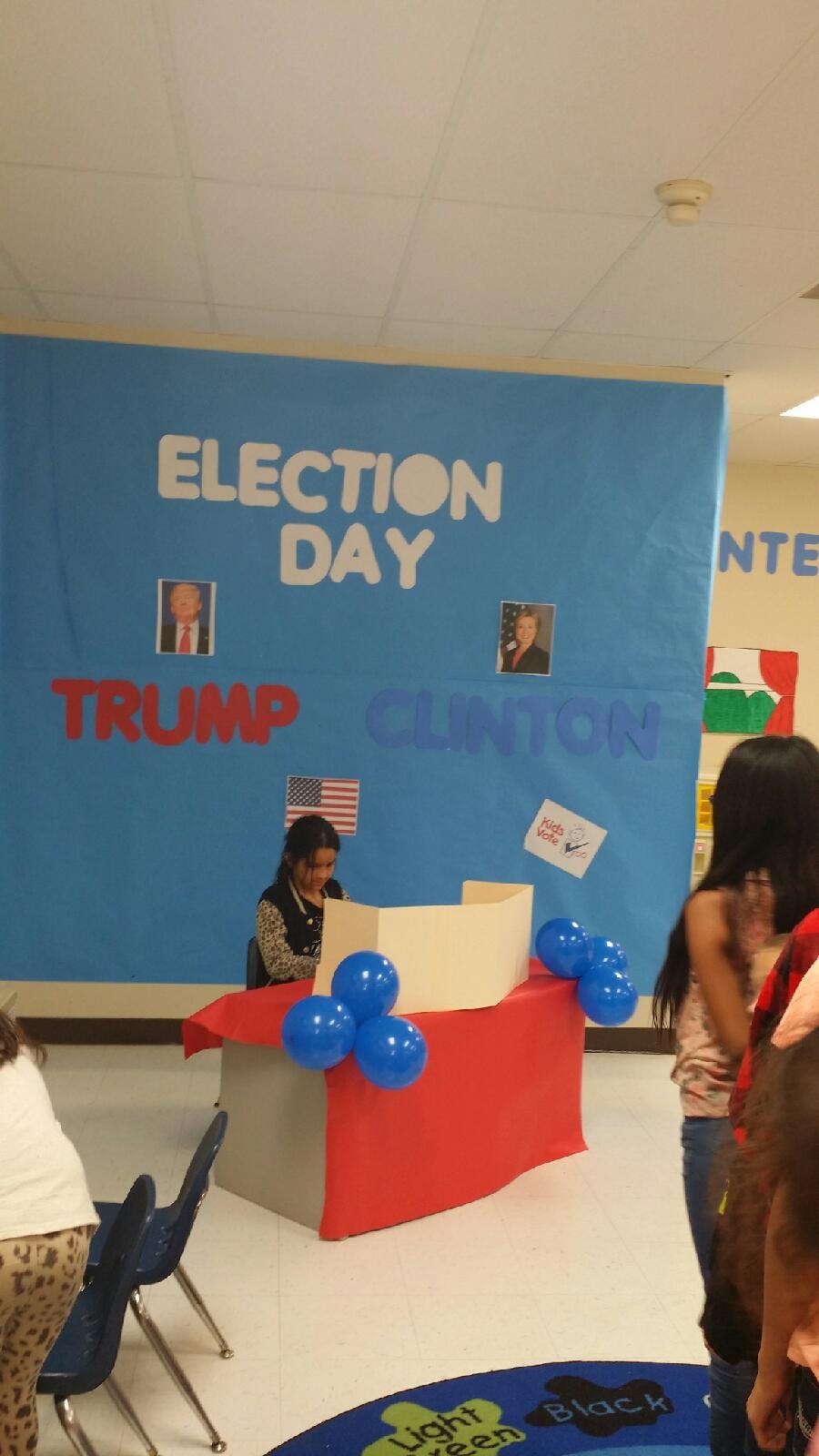 Child at a voting booth with an "Election Day" banner in the background