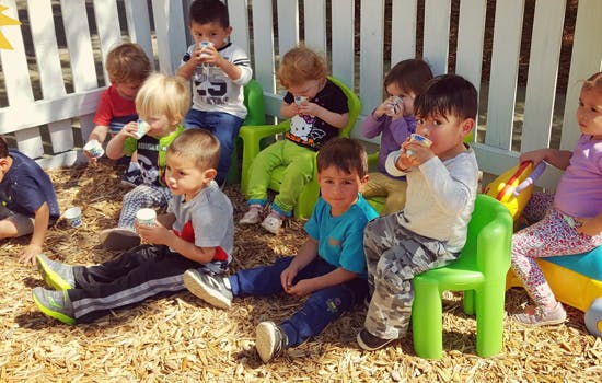 Group of children sitting outdoors drinking from cups