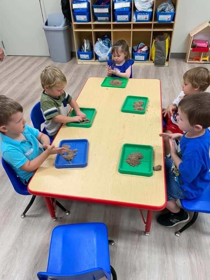 Children at a table playing with kinetic sand in trays