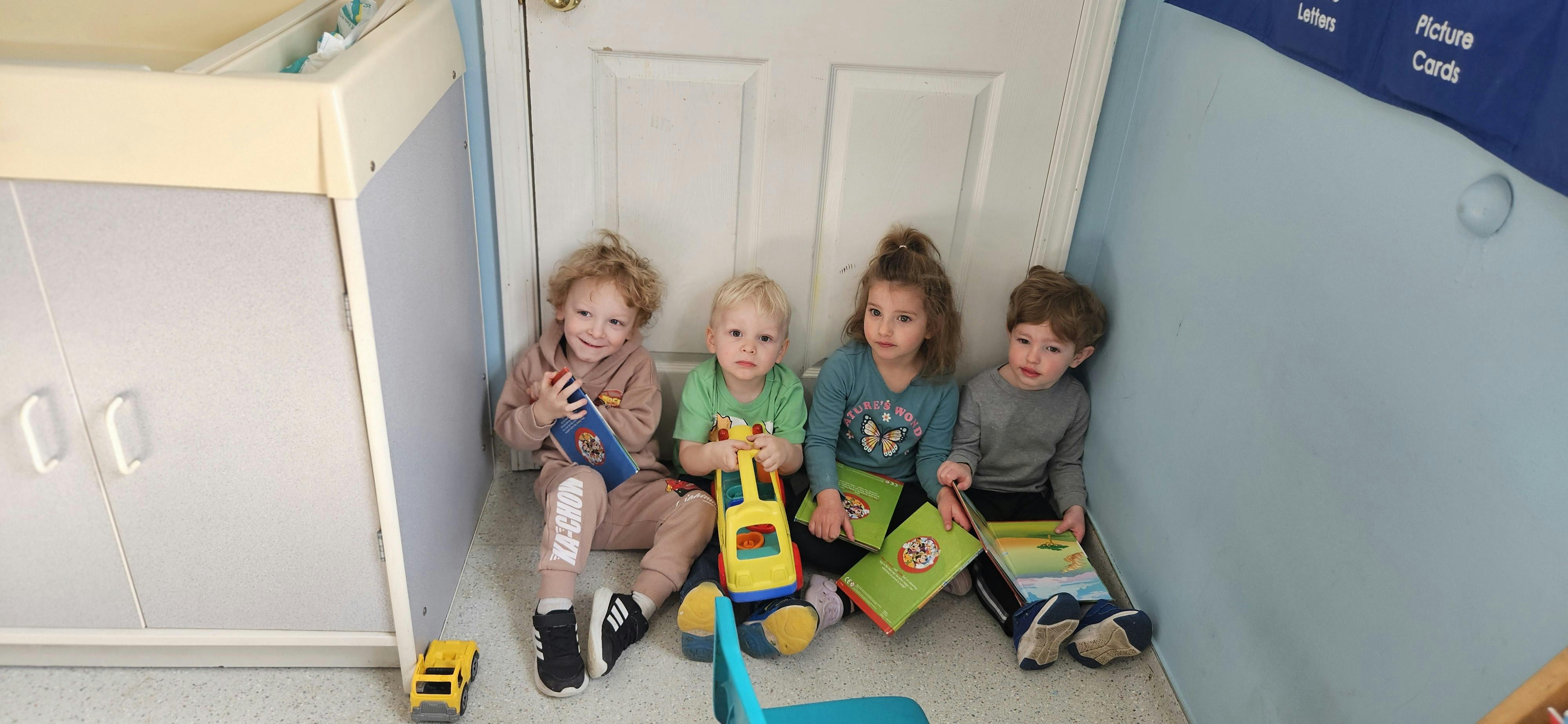 Four children sitting on the floor in a classroom playing with books and toys