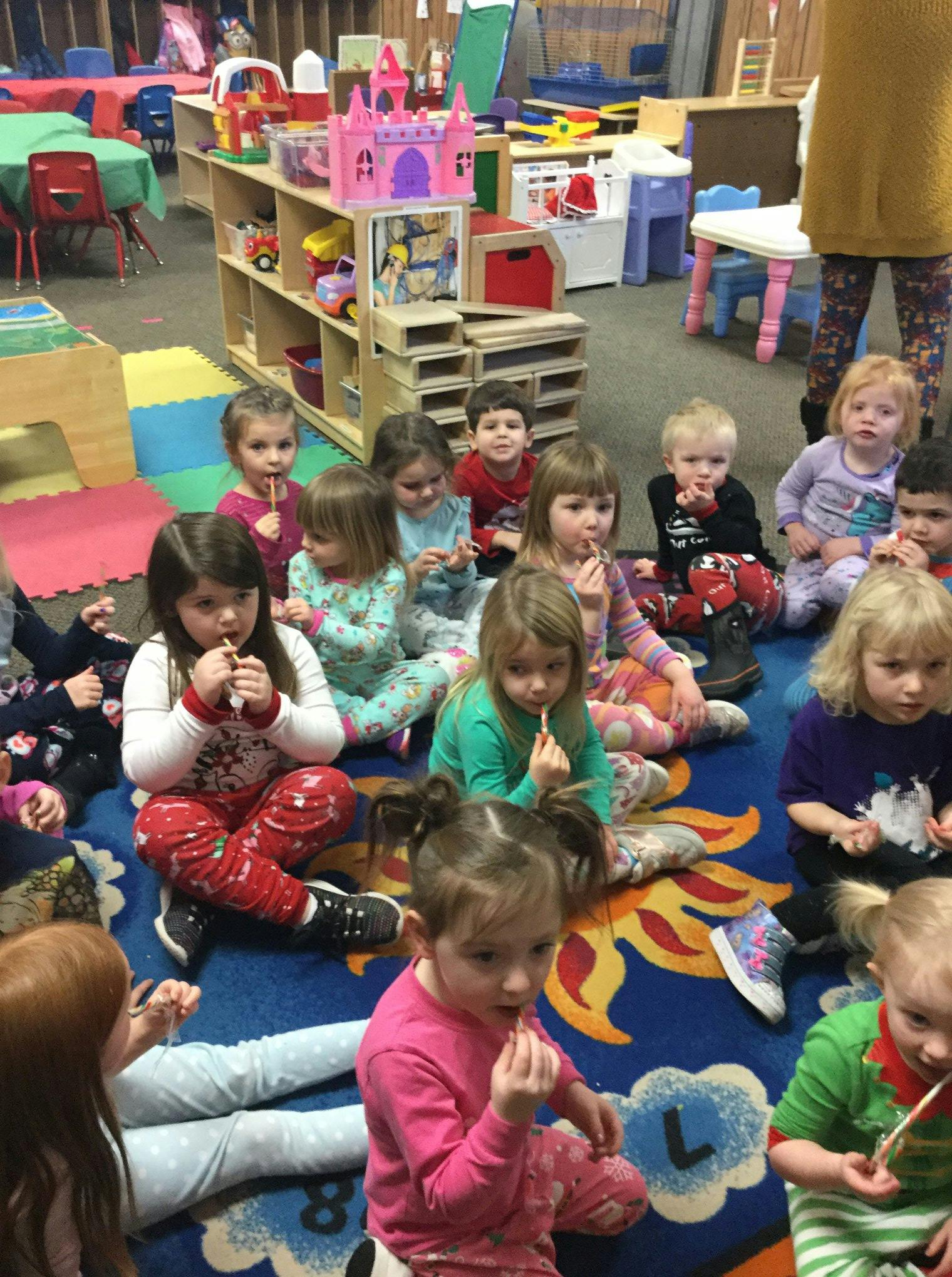 Group of children sitting on a rug, some holding lollipops