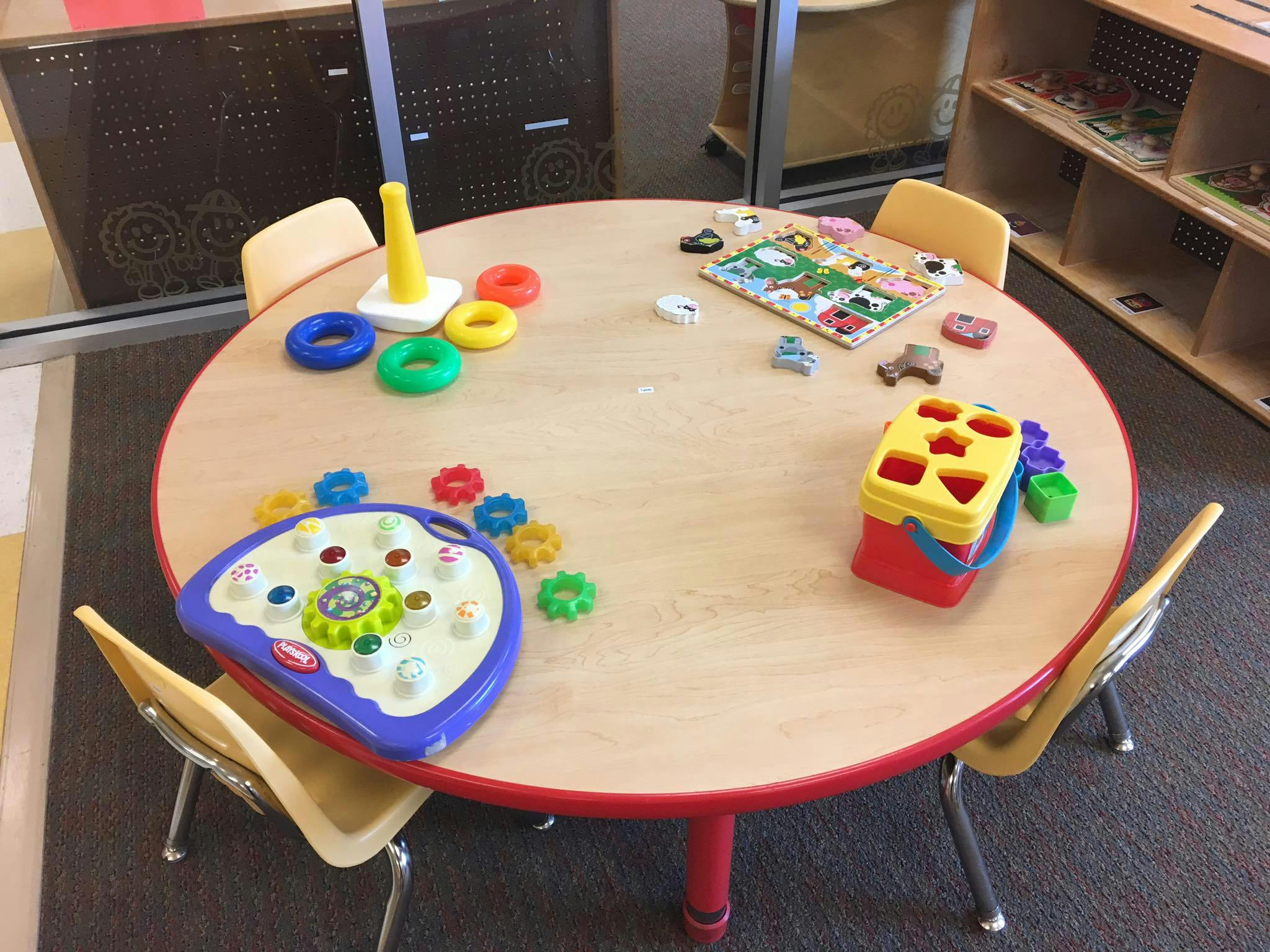 Round table with various children's toys including a shape sorter and stacking rings