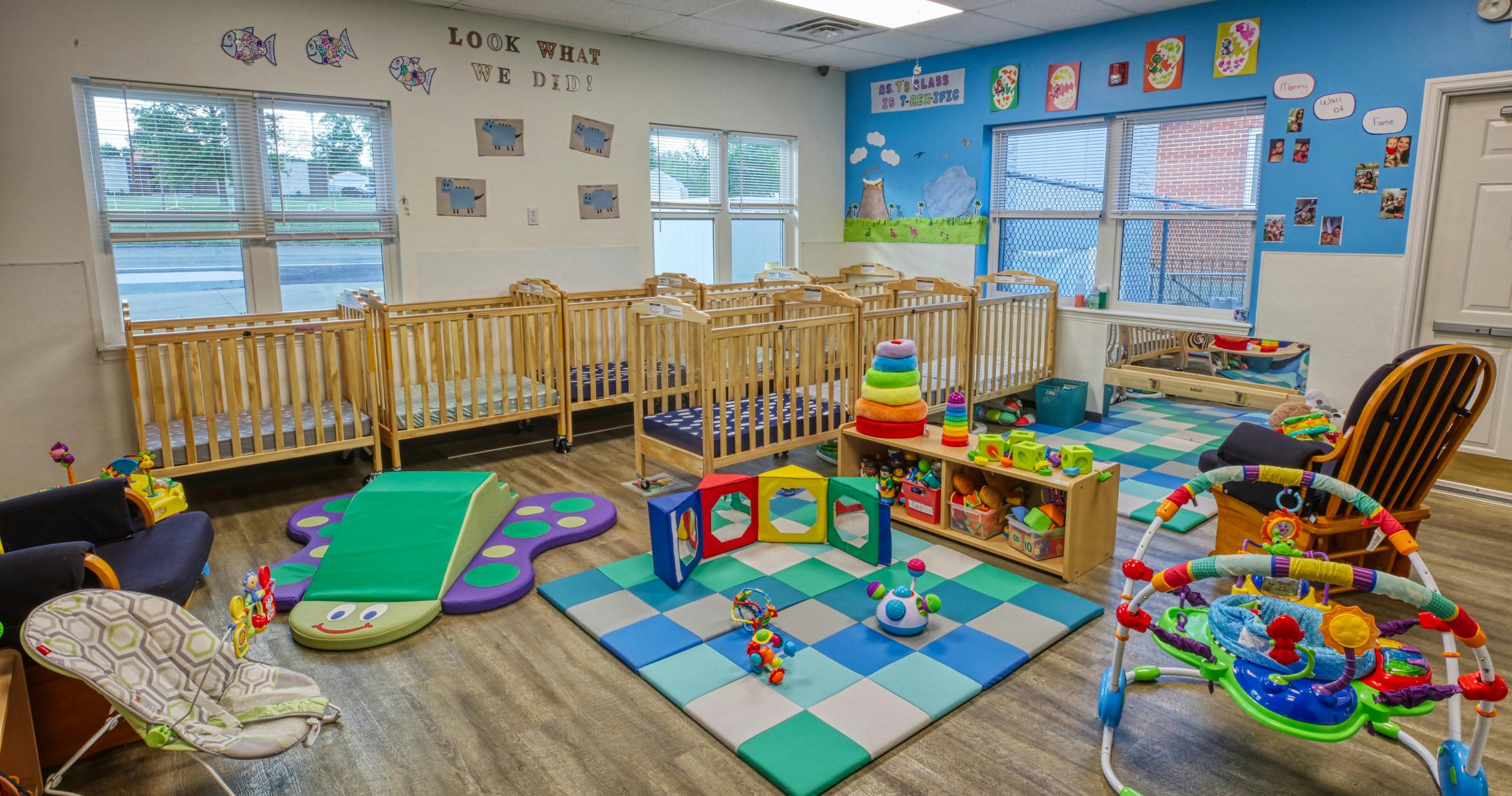 A colorful childcare classroom with several cribs, playmats, and toys