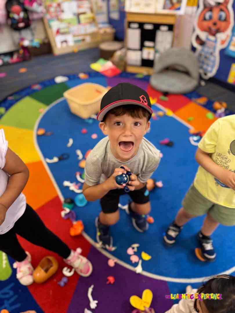 Child in a baseball cap holding a toy and looking up with mouth open