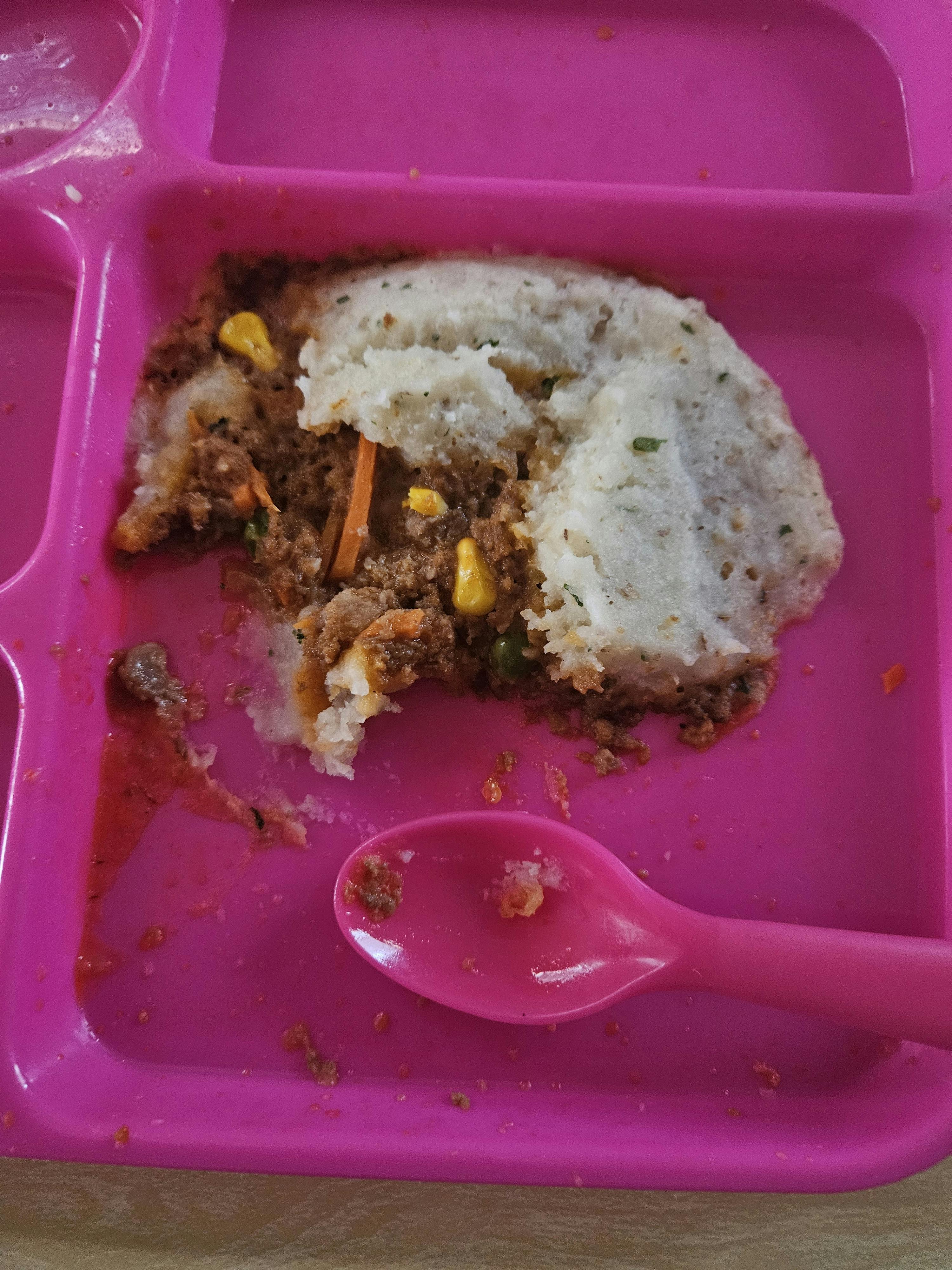 Half-eaten portion of shepherd's pie with a pink spoon in a divided container