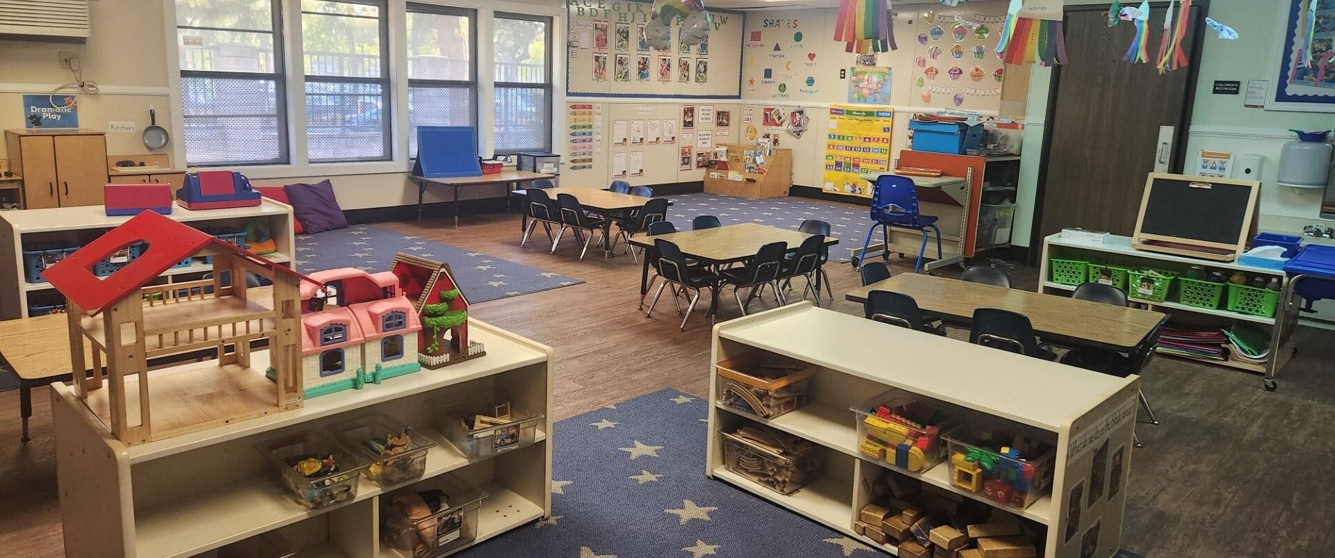 An empty classroom with tables, chairs, and play areas